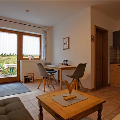 Ein gemütliches Wohnzimmer mit hellen Wänden und großen Fenstern. Es gibt einen Esstisch, eine Couch und eine moderne Küche.
