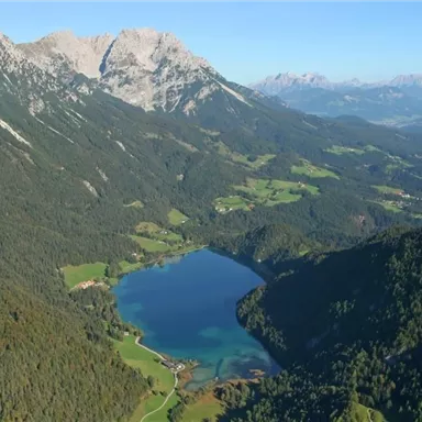 Eine atemberaubende Berglandschaft mit hohen Gipfeln und einem klaren See in der Mitte. Grüne Wiesen und Wälder umgeben die Szenerie.