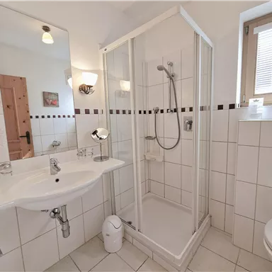 A modern bathroom with a shower, a sink, and a toilet. The walls are tiled with white tiles and there is a lot of natural light.