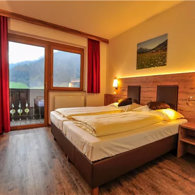 A cozy hotel room with two beds and warm wooden details. Large windows offer a beautiful view of the landscape.