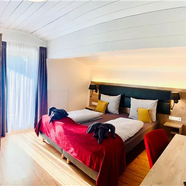 A comfortable bedroom with a large double bed and cozy pillows. The room is bright and modern with a desk and a wardrobe.