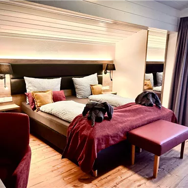 A modern bedroom with a large bed and elegant pillows. The warm colors and wooden elements create a cozy atmosphere.