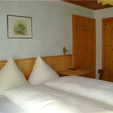 A cozy bedroom with a large double bed and pillows shaped like hills. The walls are light blue, and there are wood details as well as a small picture on the wall.