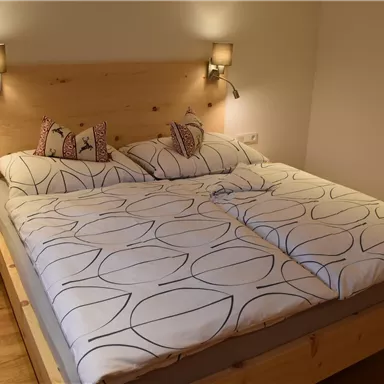 A cozy bedroom with a large double bed and wooden panelled walls. The bedding is modern and attractively designed.
