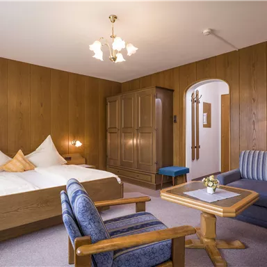 Ein gemütliches Hotelzimmer mitHolzwänden. Es verfügt über ein Doppelbett, eine Sitzecke und einen Tisch.