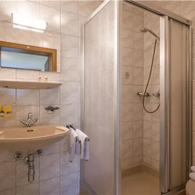 Ein einfaches Badezimmer mit Dusche, Waschbecken und Spiegel. Die Wände sind gefliest und die Ausstattung ist funktional.