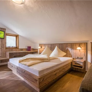 A cozy bedroom with wood paneling and a large double bed. There is a small table and windows overlooking the outdoors.