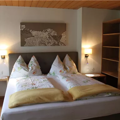 A cozy bedroom with a large double bed and decorative pillows. A painting hangs on the wall, and the decor is modern and inviting.