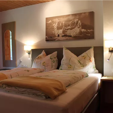 A cozy bedroom with two beds, fluffy pillows and blankets. In the background, there is a picture on the wall, and there is soft lighting.