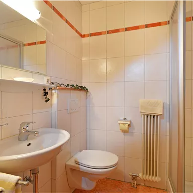 Ein modernes Badezimmer mit weißen Fliesen und orangefarbenen Akzenten. Es enthält eine Dusche, ein Waschbecken und eine Toilette.