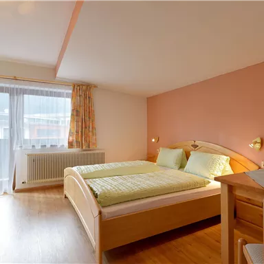 Ein gemütliches Schlafzimmer mit zwei Betten und einem Tisch. Der Raum hat große Fenster, die für natürliches Licht sorgen.