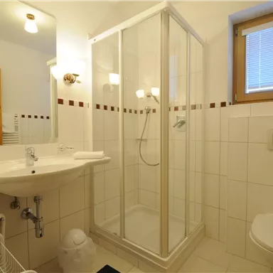 A bright bathroom with a glass shower and a sink. The walls are tiled and there is a window for natural light.