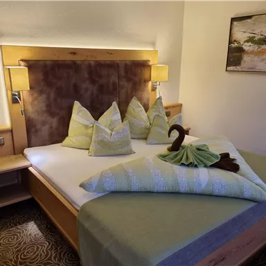 Ein gemütliches Schlafzimmer mit einem Doppelbett und dekorativen Kissen. Die warmen Farben und sanfte Beleuchtung schaffen eine einladende Atmosphäre.