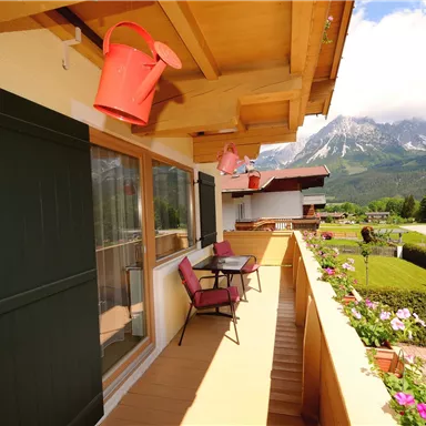 A beautiful balcony with a view of the mountains. There are two chairs and flowers on the railing.