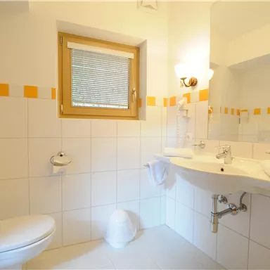 A modern bathroom with white tiles and orange accents. It features a sink, a toilet, and a large mirror.