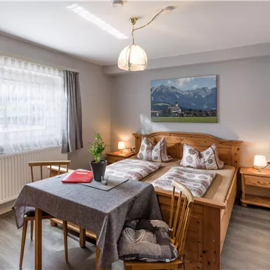 Ein gemütliches Schlafzimmer mit zwei Einzelbetten und einem kleinen Tisch. Der Raum hat ein großes Fenster und eine dekorative Wand mit einem Landschaftsbild.