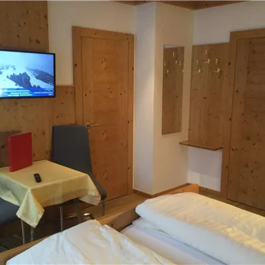 A cozy room with two beds, a table, and chairs. There is a television on the wall and a bright, inviting atmosphere.