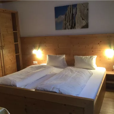 A cozy room with a large double bed and wooden paneling. A picture hangs on the wall, and there are nightstands with integrated lamps.