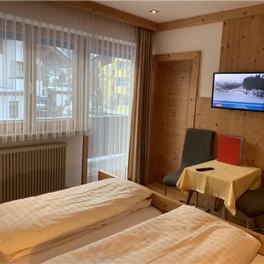 A cozy hotel room with two beds, a table and chairs. There is a window with a view outside and a television on the wall.