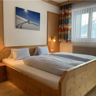 A cozy bedroom with a large wooden bed and soft colors. On the wall hangs a picture of snow and mountains.