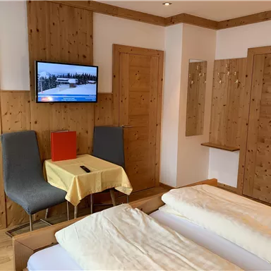 A cozy hotel room with wooden walls, a TV, and a small table. The room features two beds and an inviting atmosphere.