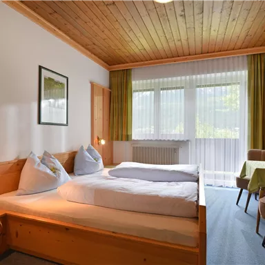 A cozy room with wood paneling and two single beds. Large windows let in plenty of natural light and offer a view of nature.