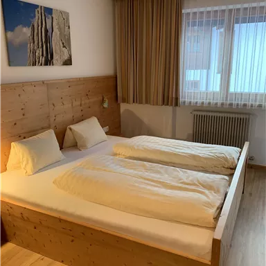 A cozy bedroom with a large double bed and wood paneling. The room has a window with curtains and an attractive wall mural.