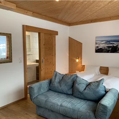 A cozy room with a double bed and a blue couch. A picture of a landscape hangs on the wall, and the room features wooden elements for a warm atmosphere.