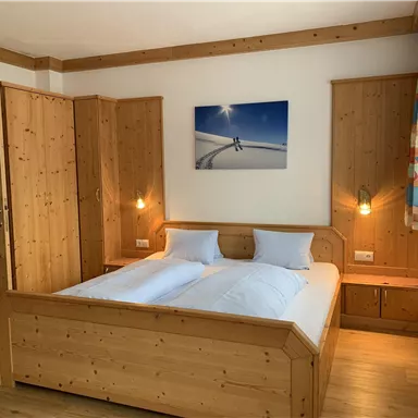 A cozy bedroom with wooden furnishings and a large double bed. A modern picture of a winter landscape hangs on the wall.