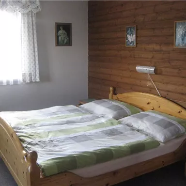 A cozy bedroom with a large wooden bed and striped bedding. The walls are wood-paneled and there is a window with curtains.