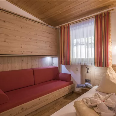 A cozy room with wooden paneling, a red sofa, and two pillows on the bed. Large windows let in a lot of light.