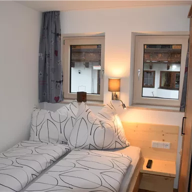A cozy bedroom with two single beds and modern pillows. The windows let in plenty of light and radiate an inviting atmosphere.