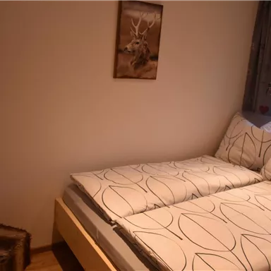 A simple bedroom with a bed and a chair. On the wall hangs a picture of a deer.