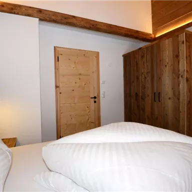 A cozy bedroom with a wooden wardrobe and a television. The bedding is white and clean, and the lighting is relaxing.