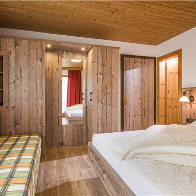 A cozy bedroom with wooden paneling and a double bed. The room features a seating area and soft lighting.