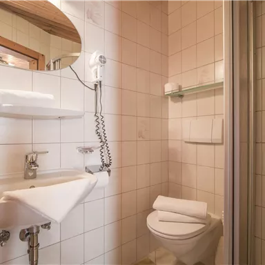 A small bathroom with white tiles. There is a sink, a shower, and a toilet.