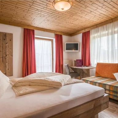 A cozy bedroom with a double bed and a couch. Large windows provide plenty of daylight and a warm atmosphere.
