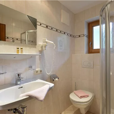 Ein modernes Badezimmer mit einer Dusche, Waschbecken und einem WC. Die Wände sind hell gefliest und ein Fenster sorgt für Tageslicht.