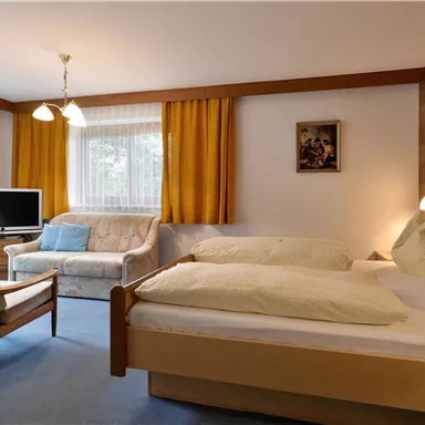 Ein gemütliches Schlafzimmer mit zwei Betten und einem Fernseher. Der Raum hat große Fenster und warme Farben.