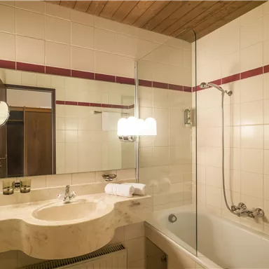 A modern bathroom with a bathtub and a separate shower. The room has bright tiles and a wooden ceiling.