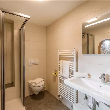 A modern bathroom with shower, sink, and large mirror. Clean tiles and towels create an inviting atmosphere.