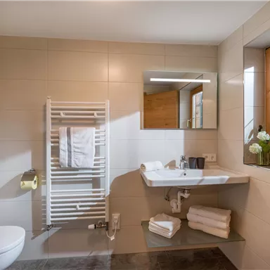A modern bathroom with a sink, a mirror, and a towel holder. Natural light comes in through the window, and clean towels are neatly arranged.
