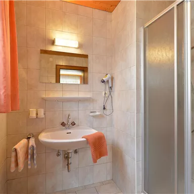 A modern bathroom with a shower and sink. It has bright tiles and orange curtains.