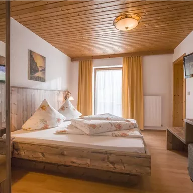A cozy bedroom with a large bed and wooden furniture. The room has windows with curtains and a wooden desk.