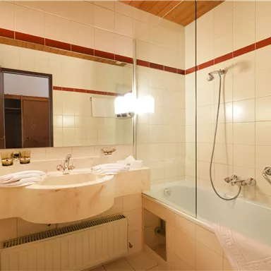 A modern bathroom with a bathtub and a sink. The walls are light tiled, and there is a large mirror surface.