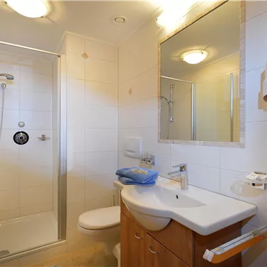 A modern bathroom with a shower, sink, and toilet. The walls are tiled in light colors and there is a large mirror.