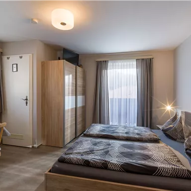Ein modernes Zimmer mit zwei Einzelbetten und einem Tisch. Große Fenster sorgen für viel Tageslicht und eine angenehme Atmosphäre.