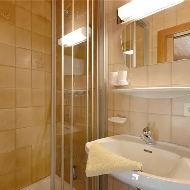 A small bathroom with a shower niche and sink. The walls are tiled in warm yellow tones.