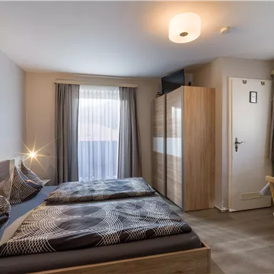 Ein modernes Zimmer mit zwei Einzelbetten, einem Schreibtisch und einem großen Fenster. Die Wände sind hell und die Einrichtung ist schlicht und elegant.