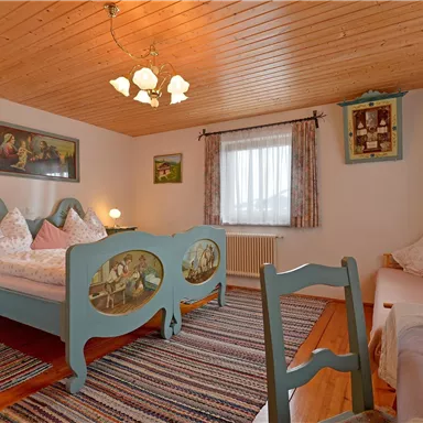 Ein gemütliches Schlafzimmer mit einem Doppelbett und hölzernem Deckenpanel. Die Wände sind mit Kunstwerken dekoriert und es gibt einen schönen Teppich sowie frische Blumen.
